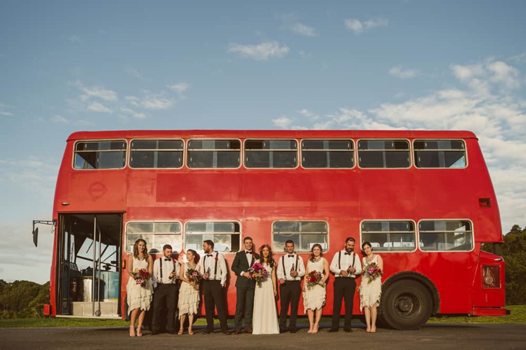 bridal party by by red double decker wedding bus