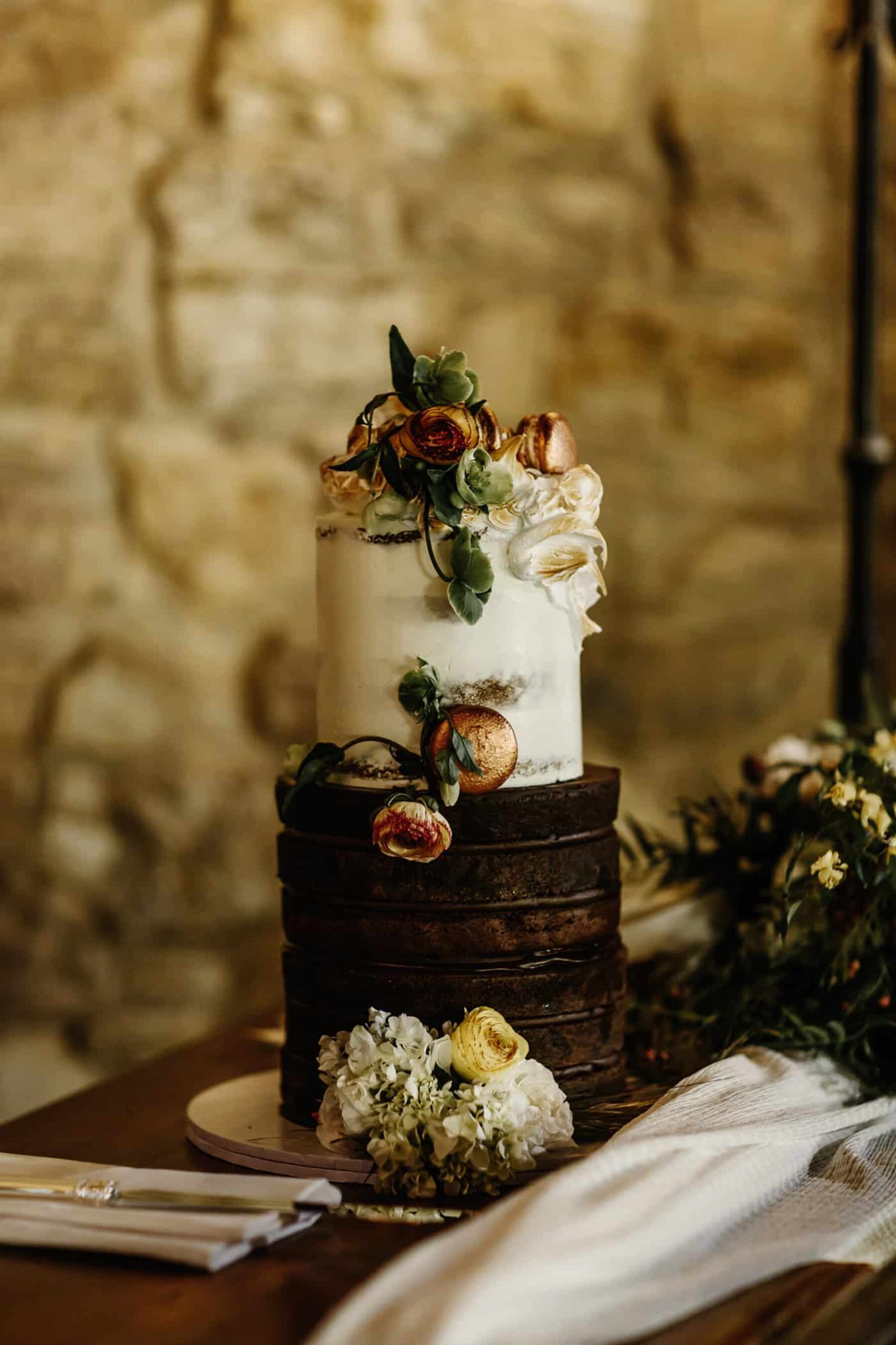 tall two-tiered naked wedding cake with rose gold macarons and fresh flowers
