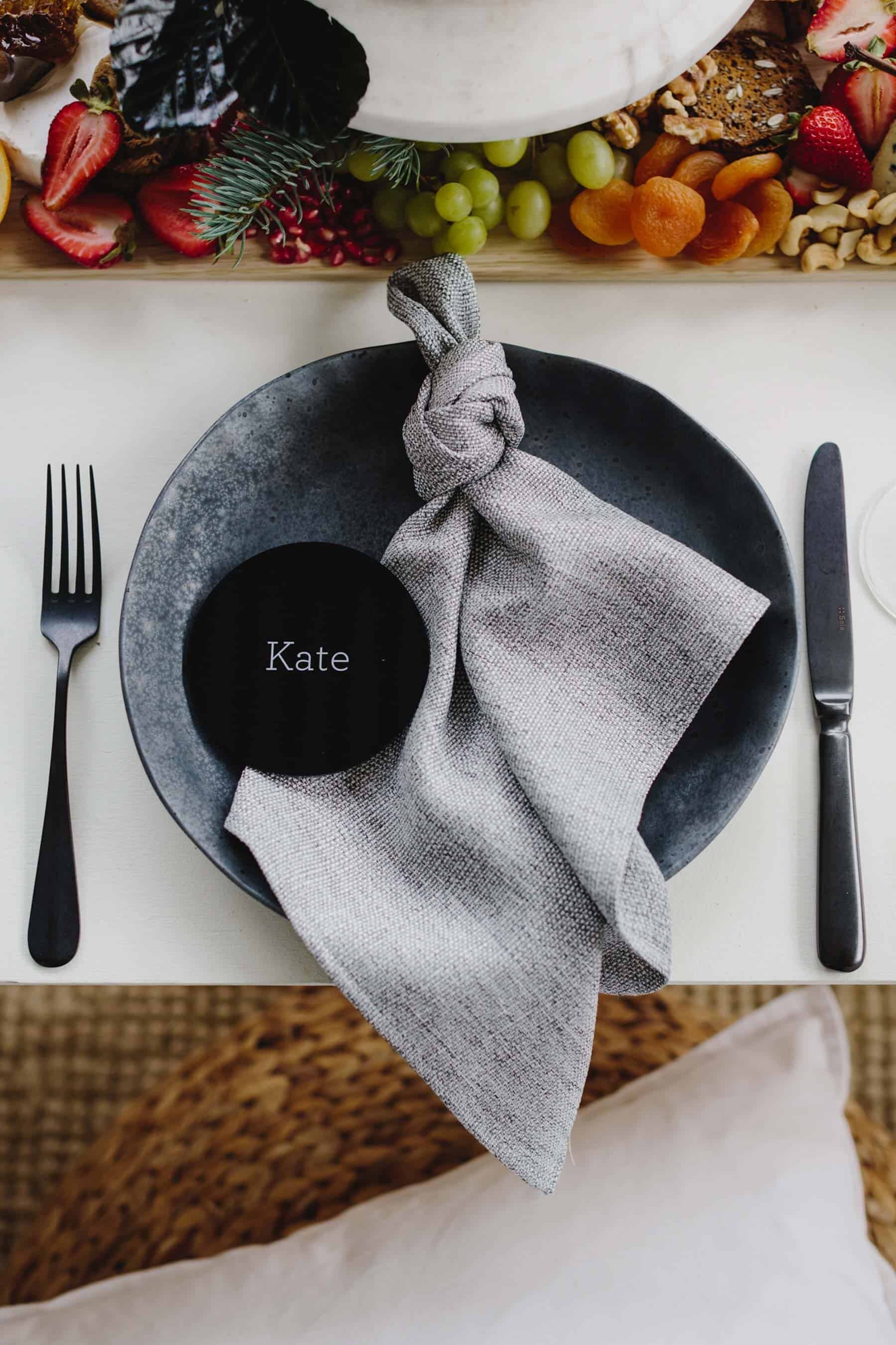 tied linen napkin on black plate with round acrylic place card