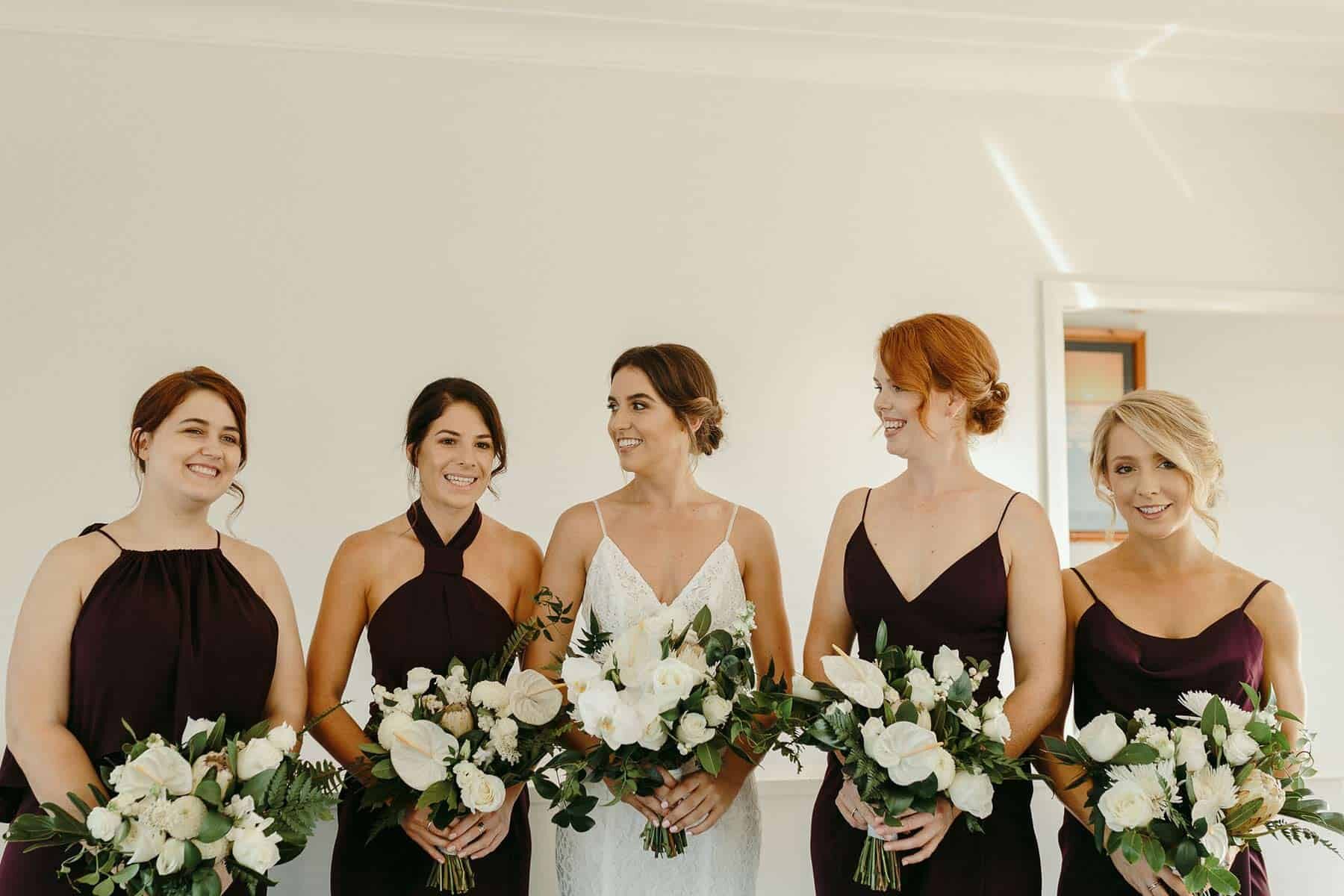 Mismatched purple bridesmaids with white and green bouquets