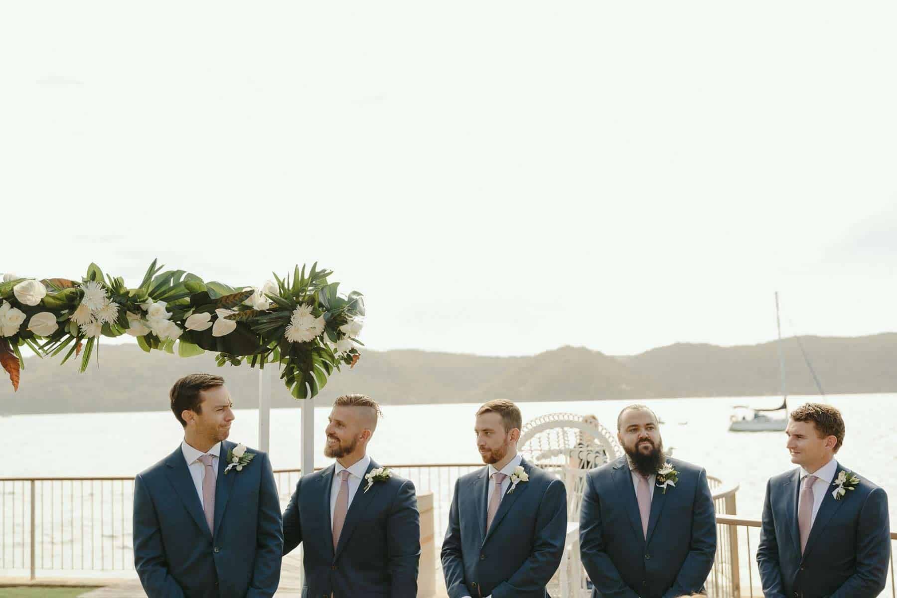 Matching groom and groomsmen in navy suits at beach wedding