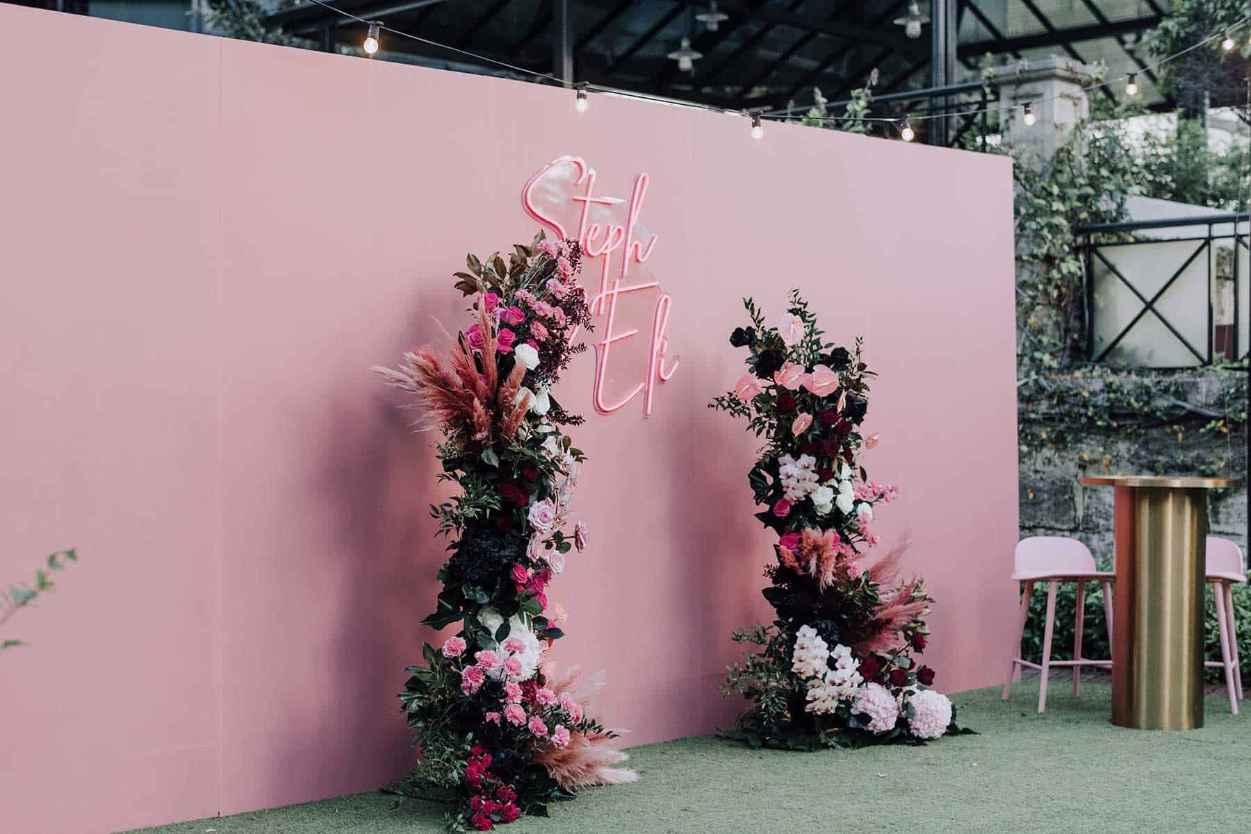 floral wedding arbour against pink wall with neon sign