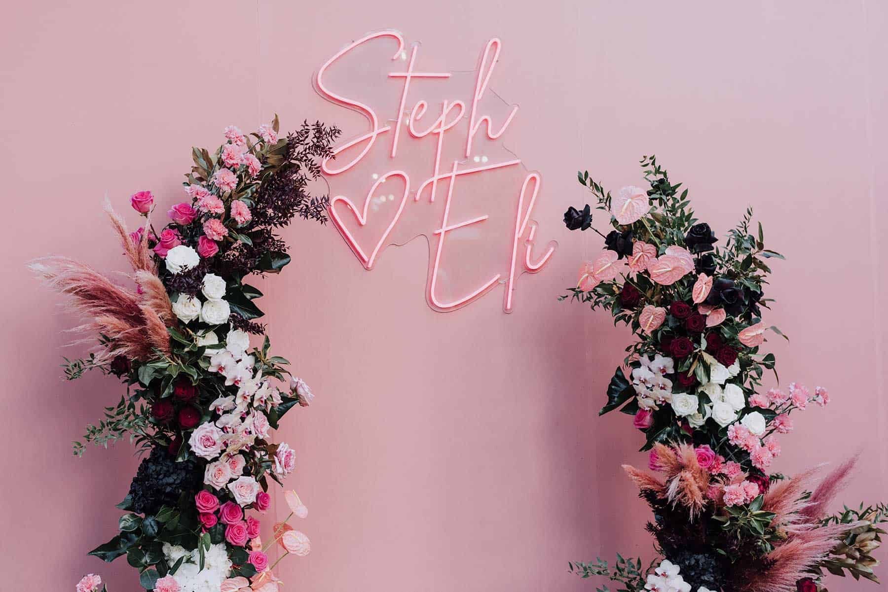 floral wedding arbour against pink wall with neon sign